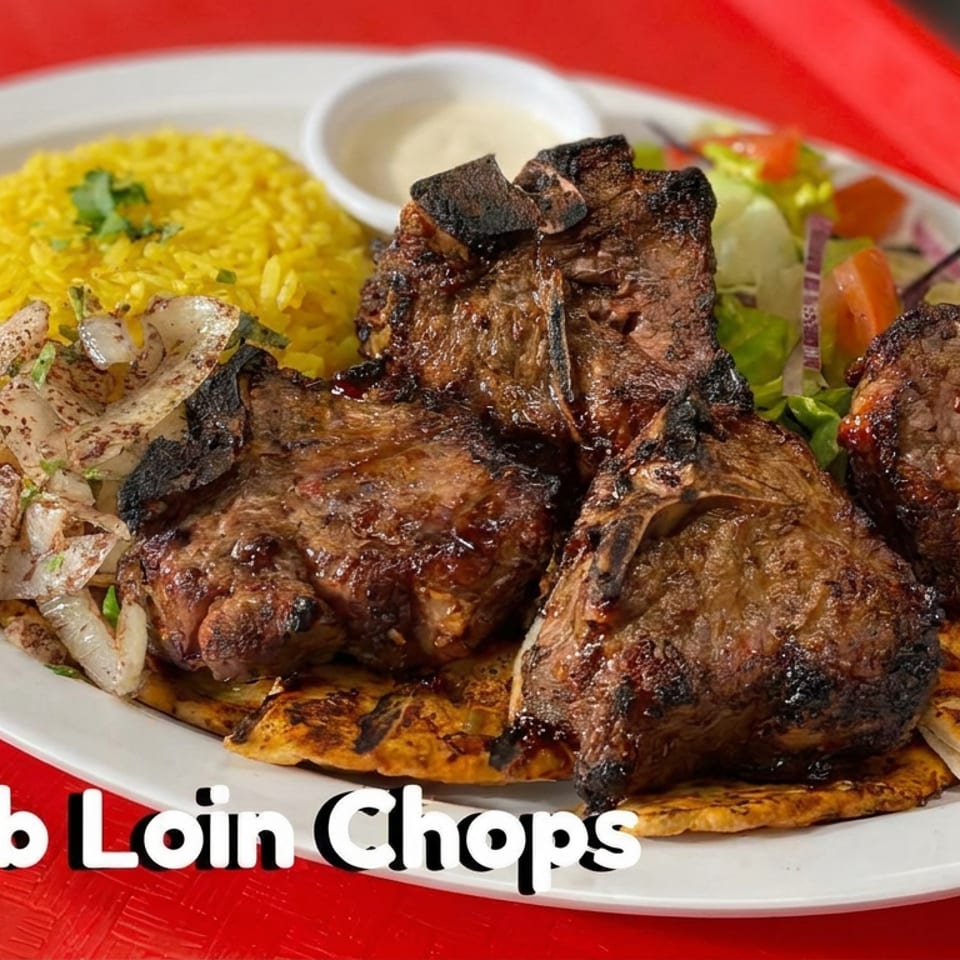 Grilled lamb loin chops served with yellow rice, plantains, onions, salad, and dipping sauce on a white plate.